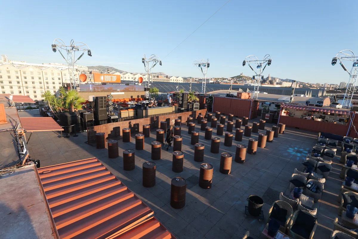 The DJ and stage end of the rooftop, with curved lighting trusses, orange banquettes, terraced orange seating steps and copper drum tables set out across the deck before opening