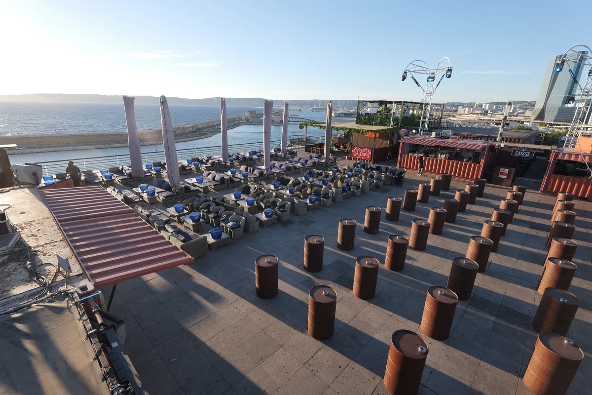 The rooftop looking west over the Mediterranean and the breakwater, copper drum tables in the foreground, lounge seating along the sea rail and the red container bars on the right